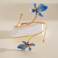 Gedetailleerde weergave van een gouden armband met twee blauwe emaille bloemen - Goud en Blauw