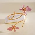 Detailweergave van een goudkleurige bovenarmband met elegante roze emaille bloemen. - Emaille Bloem Stijl / Goud en Roze