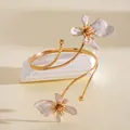 Gedetailleerd overzicht van een goudkleurige armband met witte geëmailleerde bloemen. - Goud Met Beige