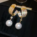 Detailopname van gouden oorbellen met schitterende zirkonia en elegante witte parels - Stijl 72 (HE32568)