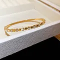 Gros plan d'un jonc en acier inoxydable doré avec cristaux sur un coffret blanc texturé - Style 5 Perles Simple / Or