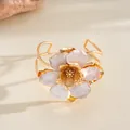 Détail d'une bague fleur dorée avec des pétales en émail irisé et bords ondulés - Bracelet manchette / Blanc