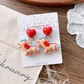 Detailed view of red heart ear clips with cartoon horse charms on white cardboard packaging - Plaid Horse Ear Clips