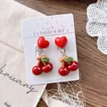Close-up of cute cherry clip-on earrings with heart studs and green leaf details - Cherry Ear Clips