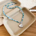Dettaglio di una collana di perle blu e bianche con un ciondolo a forma di conchiglia - Collana di Perline Sfumata (Pendente Conchiglia)