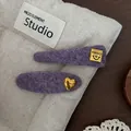 Detailed macro view of purple wool hair clips with gold metal hello and heart charms - Oval Heart Style / Purple