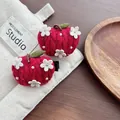 Close-up of handmade red knitted apple hair clips with white flowers and green leaves - Apple / Red
