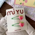 Detail view of two pink strawberry hair clips with green coating on a white display card - Strawberry