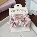 Close-up of pink plaid and satin scrunchies with dog charm and bow detail on display card - Pink Bow
