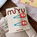 Detail of light blue metal hair clips with red apple charm on white display card - Red Apple