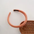 Detailansicht eines rosa Strickstirnbands mit handgefertigtem Etikett auf weißem Grund - Orange