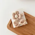 Detail of beige fabric flower and bow hair clips set on a white card over wood - Milk Tea Color Group