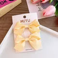Detail of two yellow ribbon bow hair clips on display card with floral background - Yellow