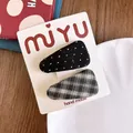 Dettaglio di due fermagli in tessuto con motivi a pois e a quadri su un cartoncino - Stile Texture Quadri Pois / Nero a Quadri