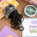 Detailed shot of bulk black elastic hair ties pouring out of a clear storage container - Plain Black Style