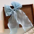 Close-up of light blue organza bow hair clip with long ribbons on wooden tray - Blue