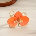 Detailed macro view of an orange enamel flower on a gold-tone open metal cuff bracelet. - Cuff Bracelet / Orange