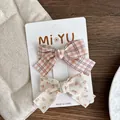 Detail of two fabric bow hair clips with floral and plaid patterns on display card - Orange Pink Bow