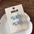 Detail of blue plaid bow hair clips with pearls on display card over ceramic plate - Transparent Duckbill Clips