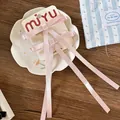 Detalle de horquillas de lazo de seda rosa en tarjeta sobre un plato de cerámica - Rosa Claro