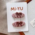 Détail de deux barrettes en tissu à carreaux roses avec nœuds brodés sur fond beige - Style Ensemble Nœud