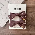 Détail de deux barrettes à nœuds en tissu à pois marron avec étiquettes dorées - Nœud à Pois (2 Pièces)