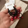 Dettaglio di elastici per capelli con ciliegia rossa e corde nere elastiche su carta bianca - Rosso
