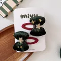 Dettaglio di fermagli natalizi con fiocchi di velluto e stelle dorate su scheda espositiva - Fermagli BB / Verde