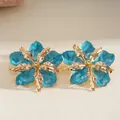Macro shot of elegant gold-tone metal flower earrings with blue marbled enamel petals - Steel Post Studs / Cyan