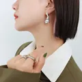 Minimalistische set van zilveren golvende oorbellen en geometrische ring op een model - Staalkleur