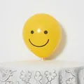 Close-up of yellow matte latex balloon with black smiley face on a white stand - Yellow Smiley Face
