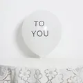 Detail of matte white 10-inch latex balloon with grey TO YOU text on lace tablecloth - White To You Print