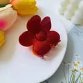 Detailed view of elegant red flower hair claw clip on a white tray with tulip decor - Red Orange Contrast