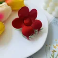 Close-up of a glossy red flower hair claw clip displayed on a white ceramic plate - Red and Light Green