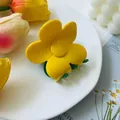 Detail shot of a yellow five-petal flower hair claw clip with green teeth on a white tray - Yellow and Green