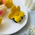 Detailed macro view of a matte yellow flower hair claw clip on a white decorative plate - Yellow Blue Block