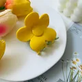 Close-up of a yellow flower hair claw clip on a decorative white ceramic plate - Yellow and Light Green
