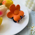 Detailed view of orange flower claw clip with blue teeth on a stylish white plate - Orange/Blue
