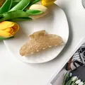 Detail shot of large cream acetate hair claw clip with shell texture on ceramic plate - Yellow Floral