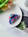 Bunte Haarklammer mit blau-rosa Streifen auf einem weißen Teller im Lifestyle-Look - Rot Weiß Gestreift