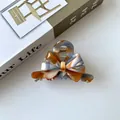 Macro shot of marble textured acetate hair claw clip with elegant metal spring detail - Maillard Coffee Plaid