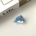 Gros plan d'une mini pince à cheveux dauphin bleue pailletée en acétate sur un livre - Petit Dauphin / 2cm