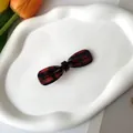 Detailed top view of red and black plaid bow hair clip on a white ceramic tray with tulips - Red Plaid