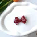 Primer plano de un pasador de pelo con lazo rojo oscuro brillante en bandeja blanca - Clip de Pico de Pato Rojo