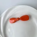 Minimalistische orangefarbene Schleifen-Haarspange aus glänzendem Harz in weißer Schale - Orange