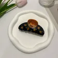 Detail of acetate hair claw clip with golden stars and sun face on marble texture - Sun