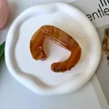 Detail of amber tortoiseshell claw clip with Can lettering on white ceramic plate - Letter C(Can) / 9x6.5cm / Coffee