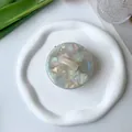 Detailed top view of a round pearlescent acetate hair claw on a white ceramic plate - Pearl White