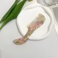 Detailed view of pink marble acetate wide-tooth comb on a decorative ceramic tray - Yellow-Pink