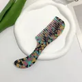 Close-up of marble texture acetate hair comb on white ceramic plate with green leaves - Rainbow
